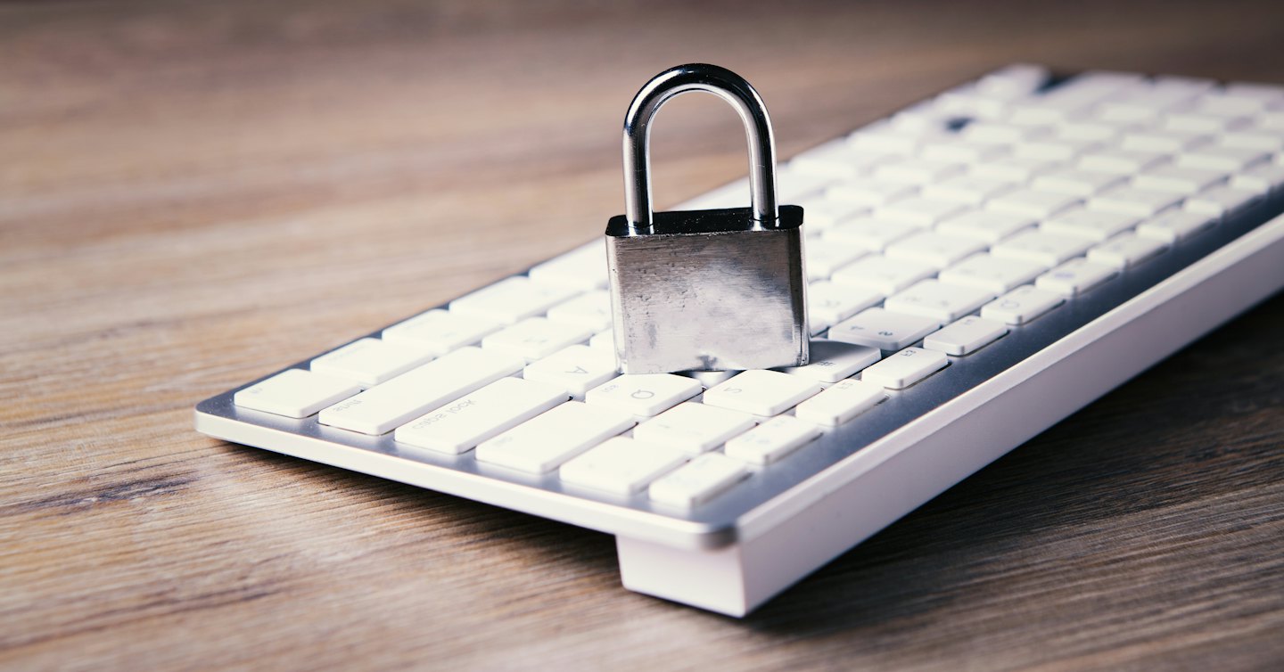 Un candado plateado descansa sobre un teclado de computadora blanco.